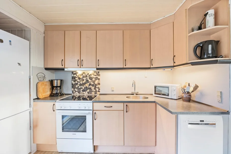 A compact kitchen with light wood cabinets, a stove, and countertop appliances.