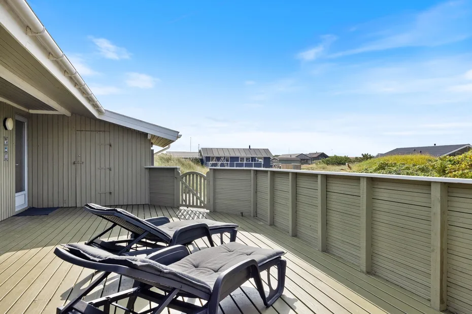 A sunny outdoor deck with cushioned lounge seating and a privacy fence.