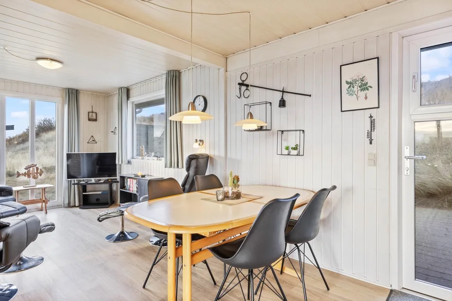 A bright dining area with a wooden table and dark chairs beside large windows.