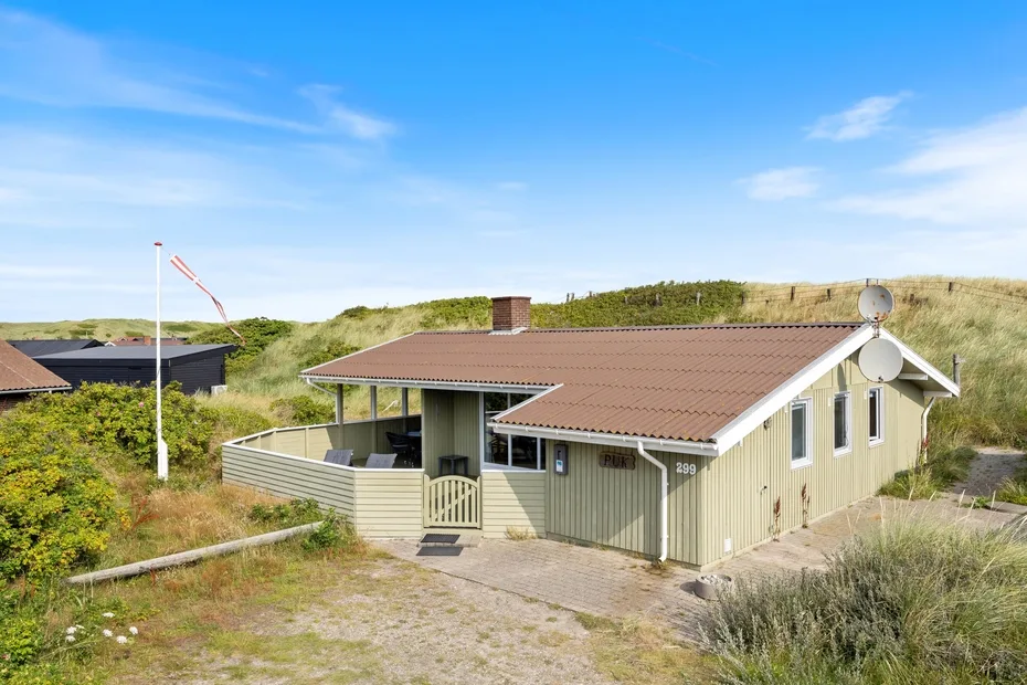 A low house sits among grassy dunes beneath a clear blue sky.
