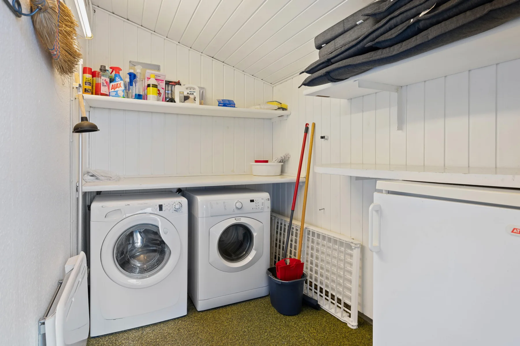 A laundry room with a washing machine, dryer, and cleaning supplies on a shelf.