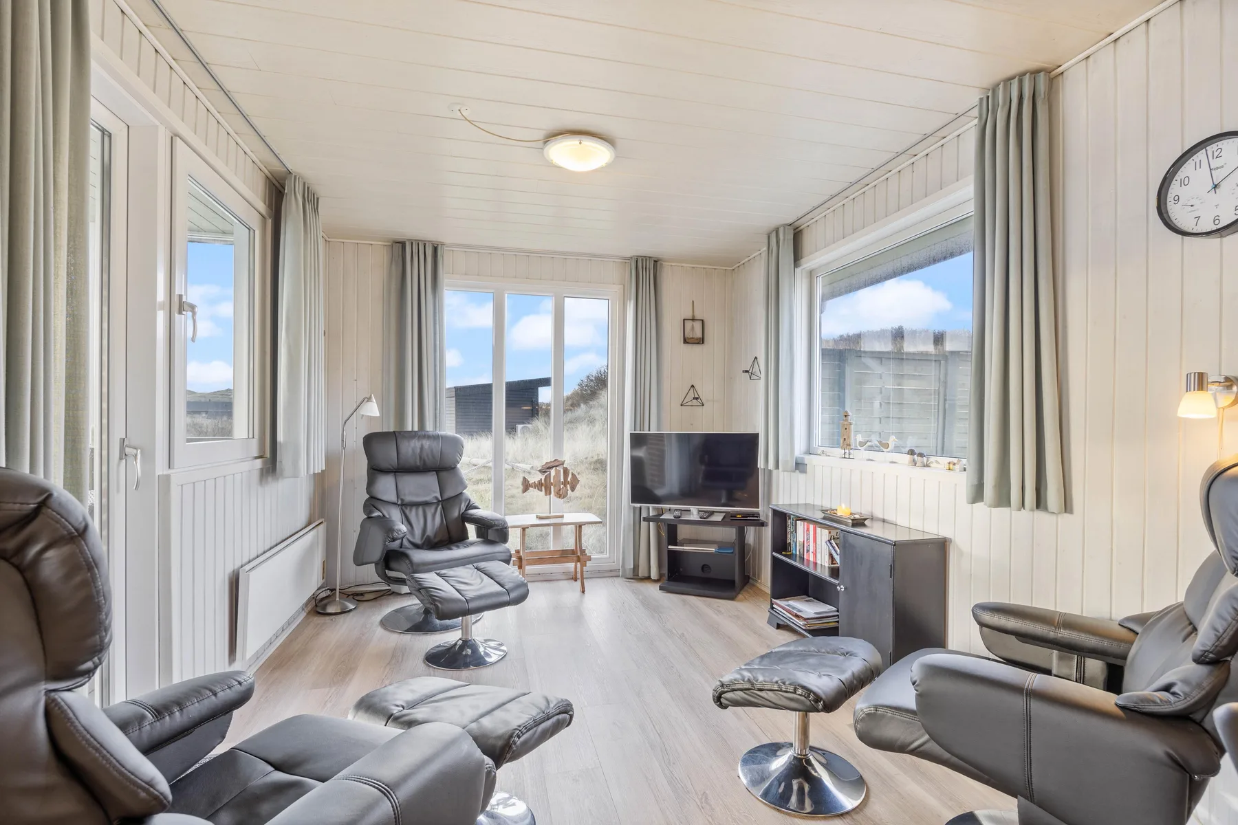 A bright living room with seating facing a television and large windows.