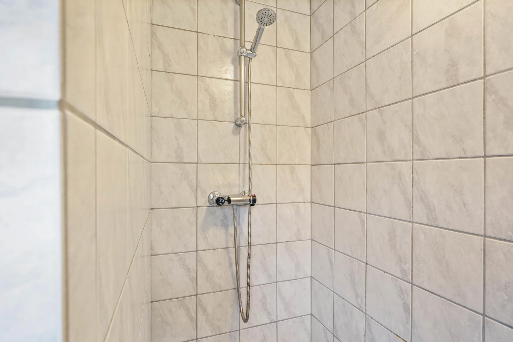 A tiled shower area with a wall-mounted showerhead and controls.