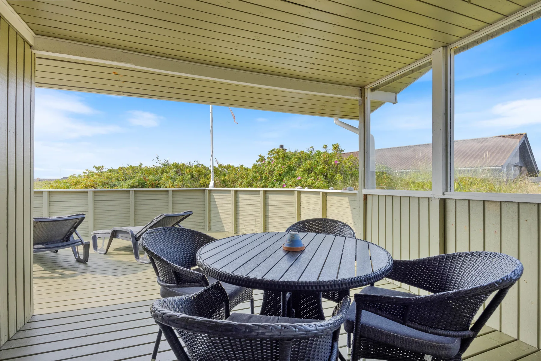 A covered outdoor seating area with a round table and woven chairs.