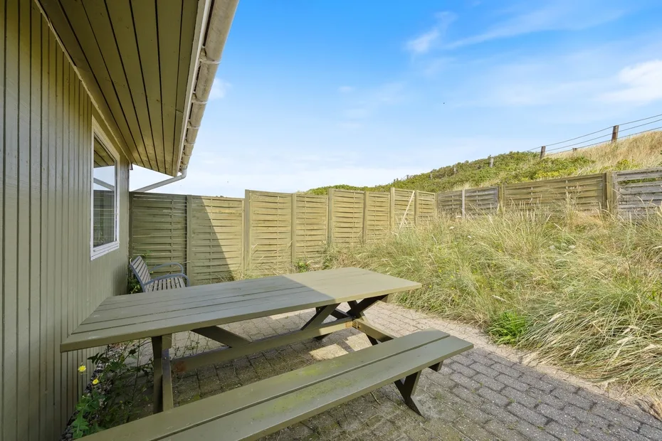 An outdoor patio with a picnic table beside a wooden fence and tall grasses.