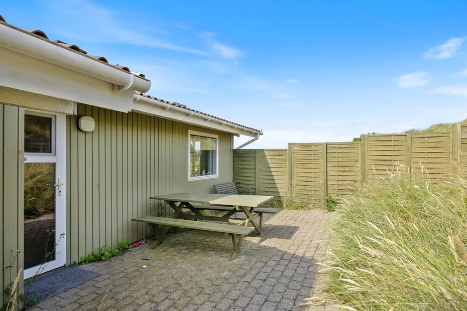 A paved outdoor patio beside a house, with a picnic table and wooden fencing.