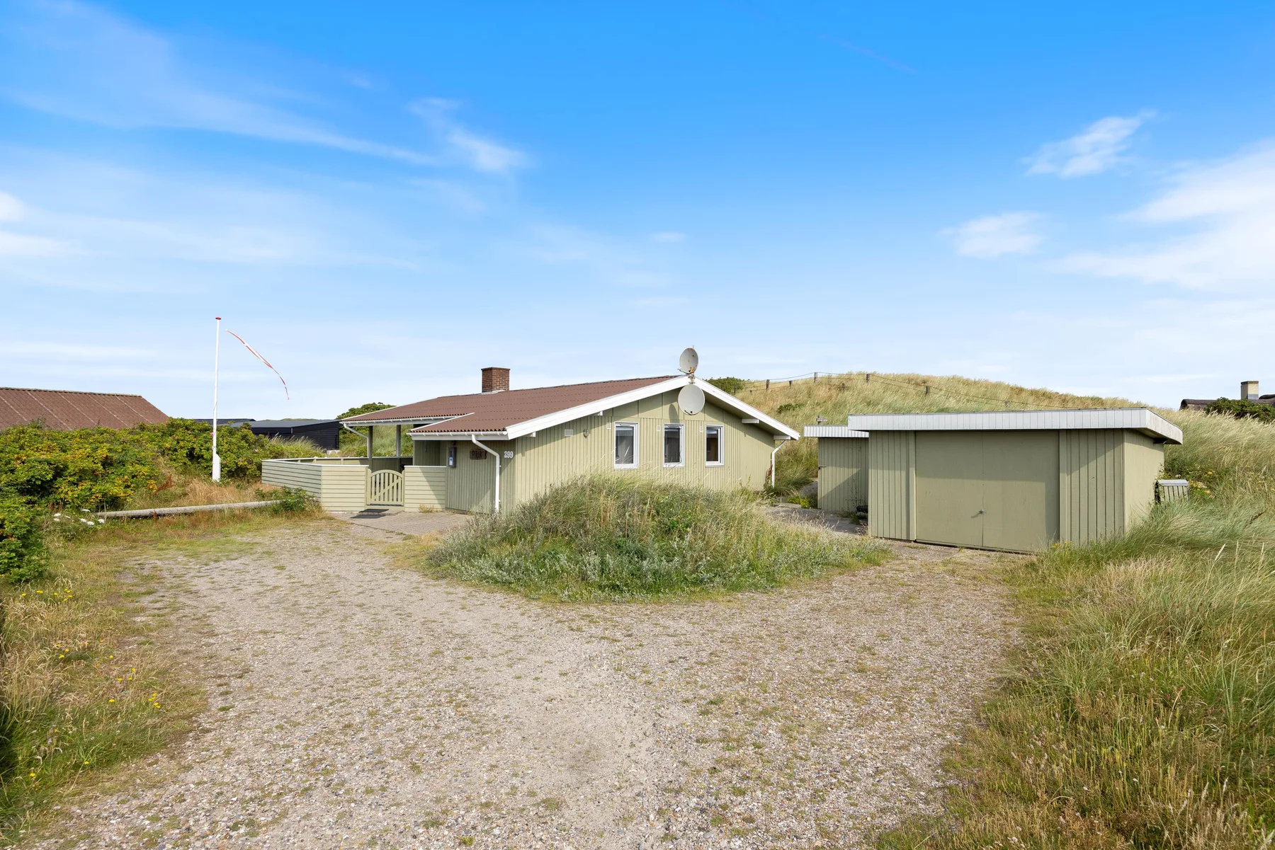 A single-story house and detached outbuilding stand beside a gravel drive in grassy surroundings.