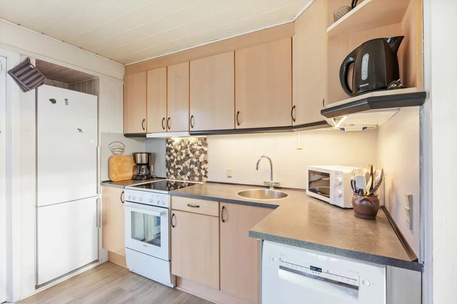 A compact kitchen with light wood cabinets, a refrigerator, and countertop appliances.