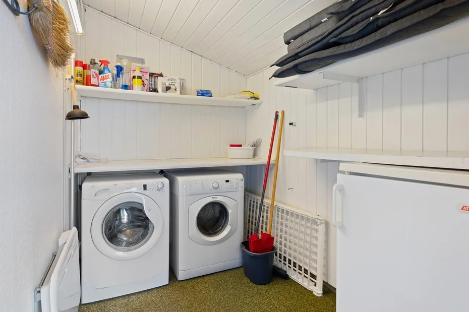 A laundry room with two washing machines, cleaning supplies, and folded linens on an upper shelf.