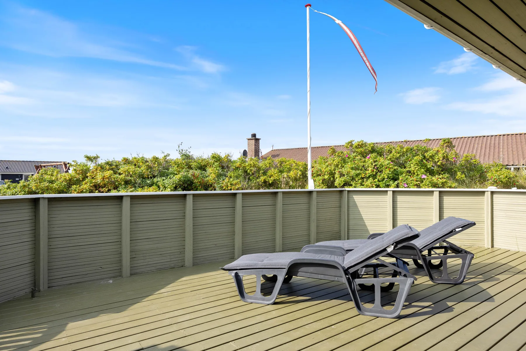 A sunlit outdoor deck with reclining lounge chairs beside a tall privacy fence.