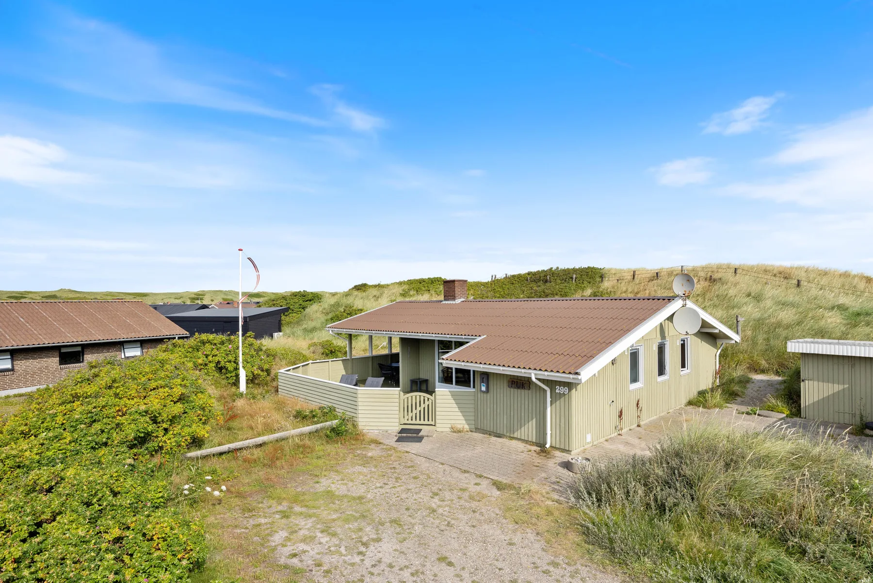 A low house sits among grassy dunes beneath a clear blue sky.
