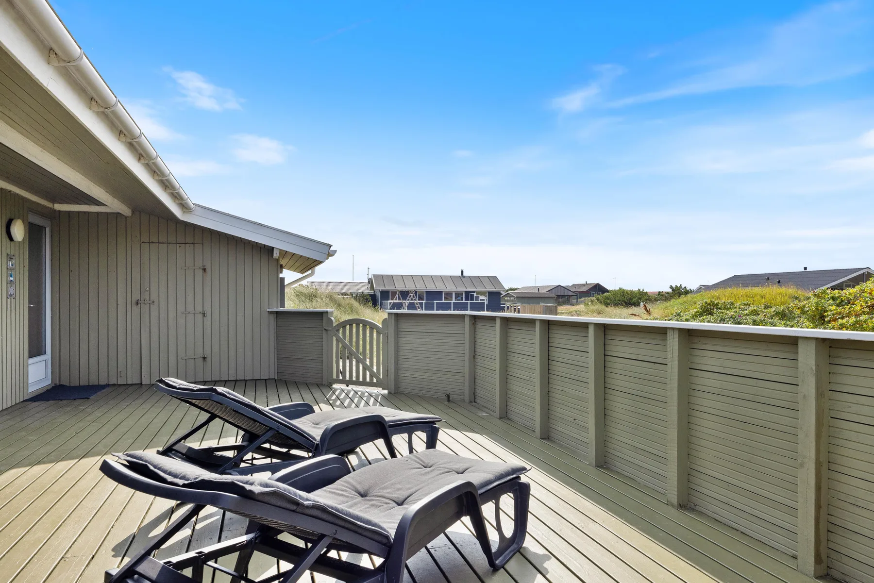 A wooden deck with lounge seating and a high fence under a clear sky.