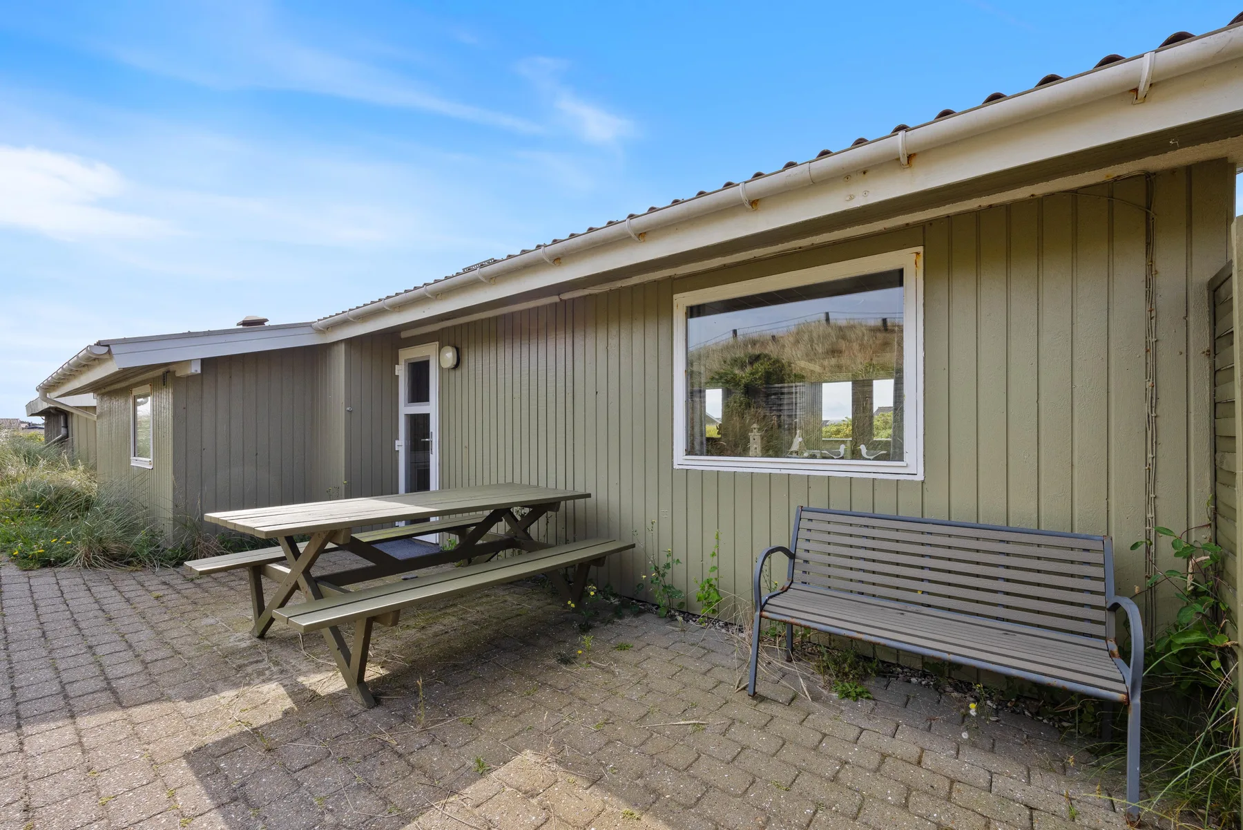 An outdoor patio beside a house features picnic seating and a bench.