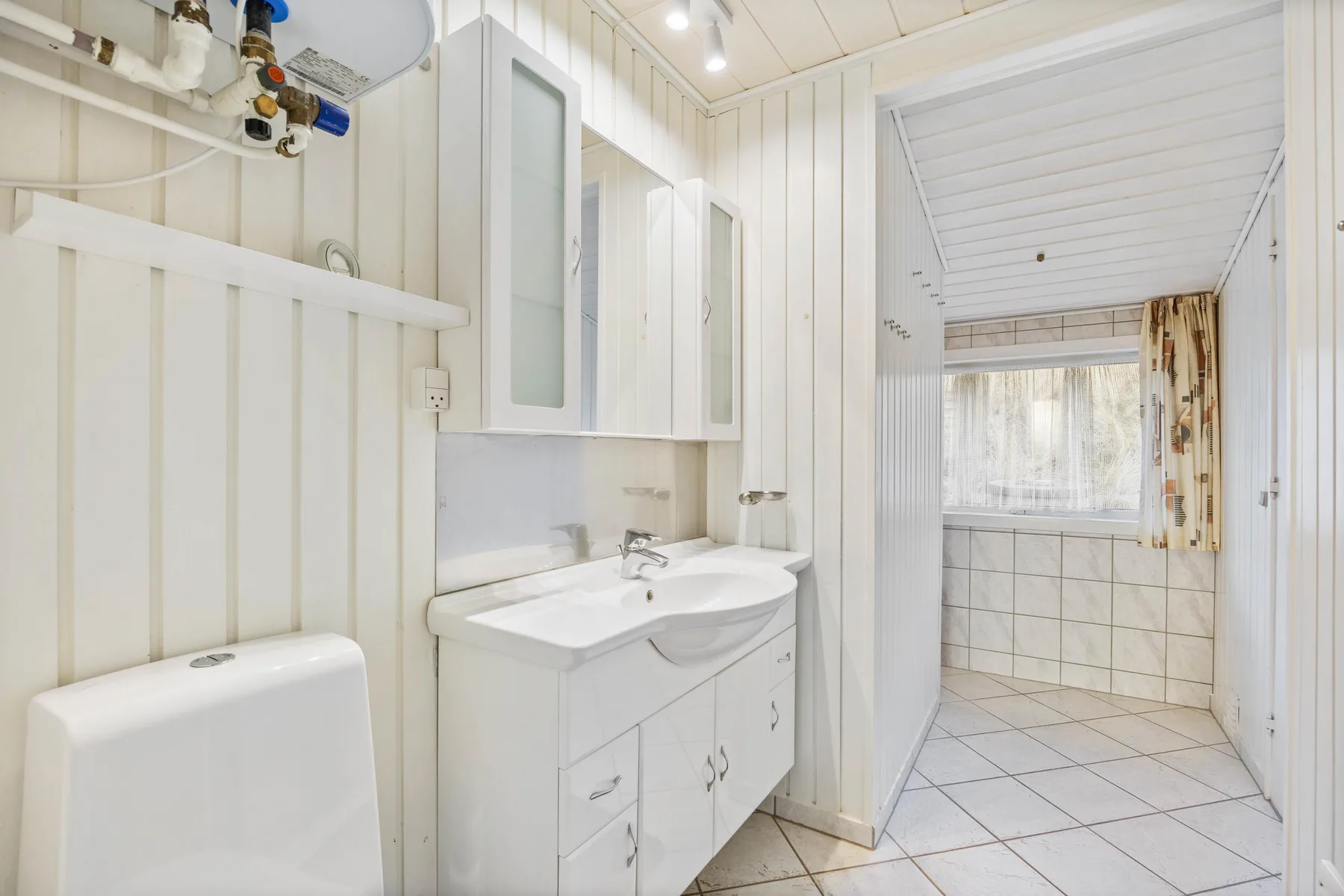 A bright bathroom with a sink vanity and a curtained window.