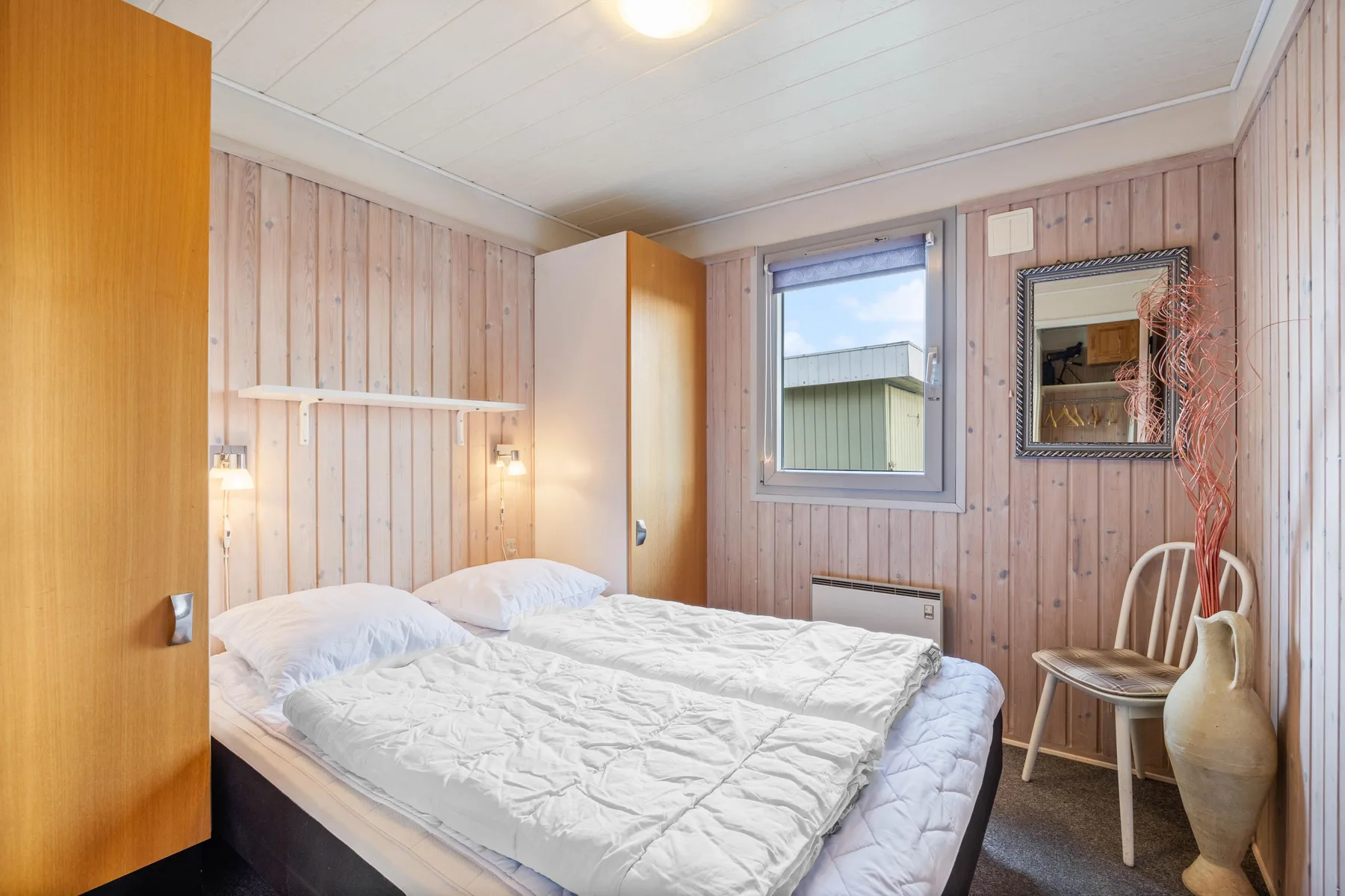 A bedroom with a bed, pale wood-paneled walls, and a window.