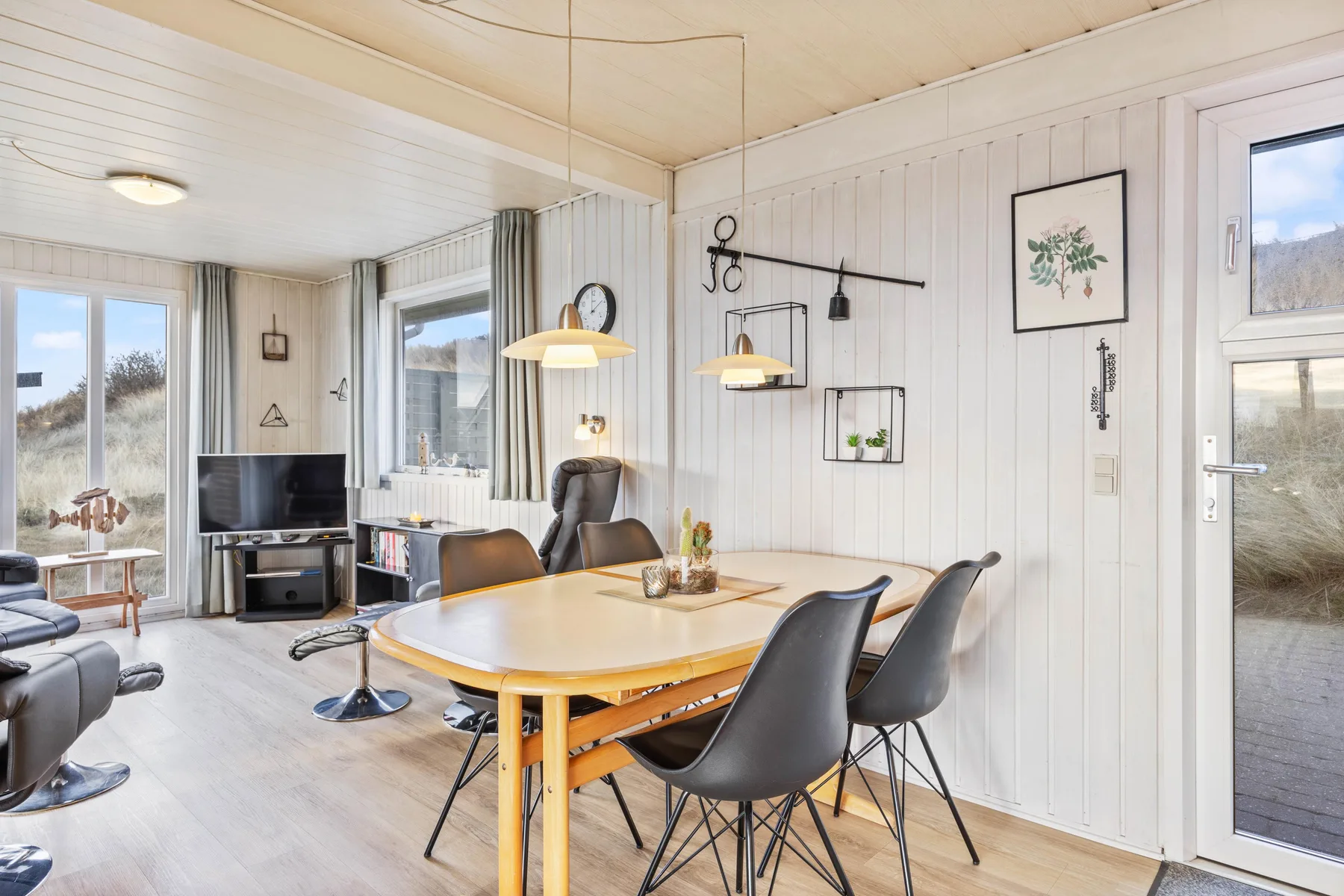 A bright dining area features a wooden table and dark seating beside large windows.