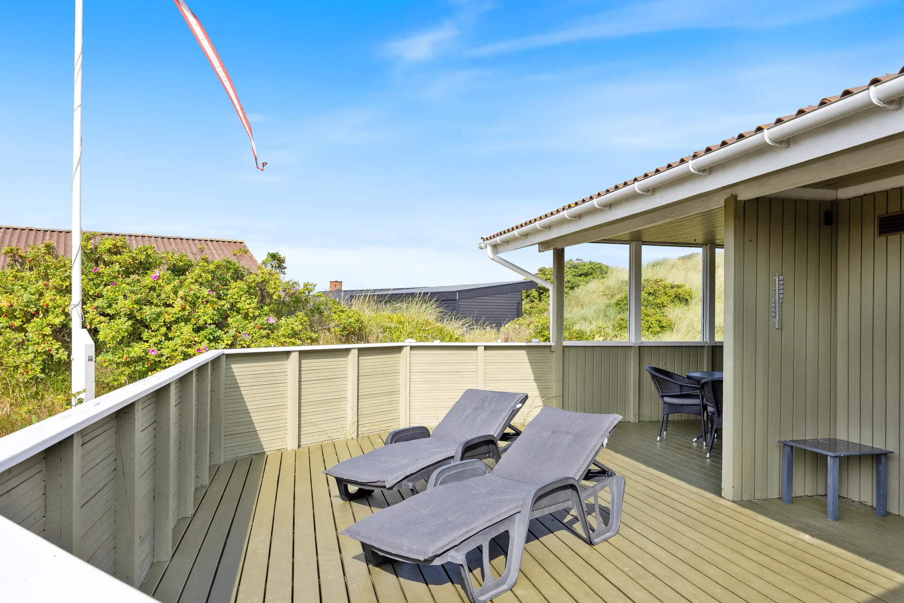 A wooden outdoor deck with reclining seating beside a house.