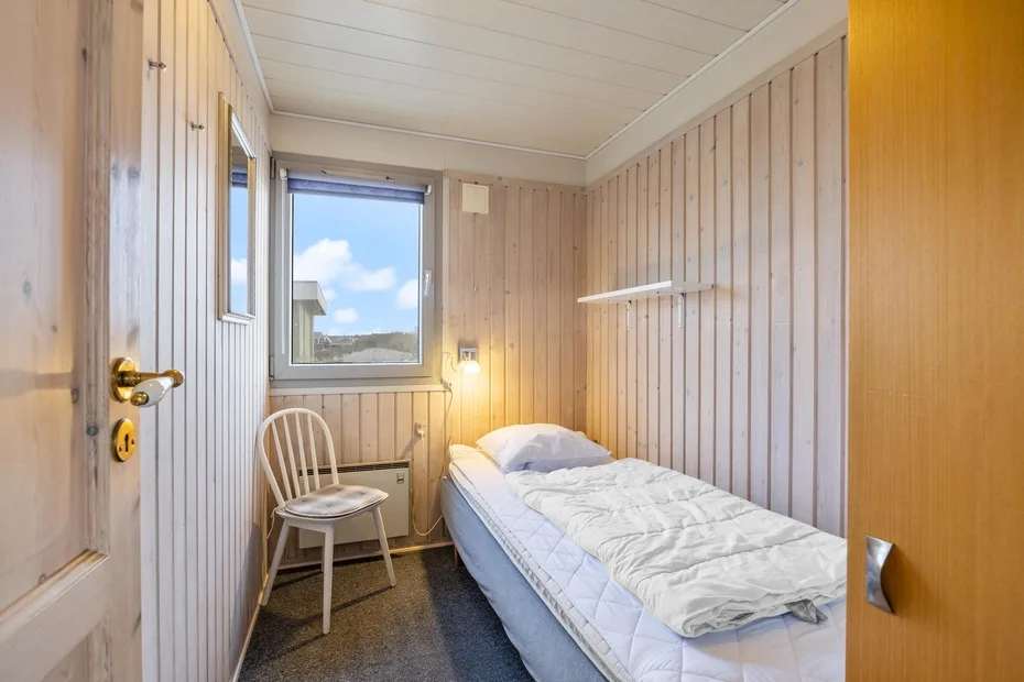 A compact bedroom with a single bed, a chair, and a window.