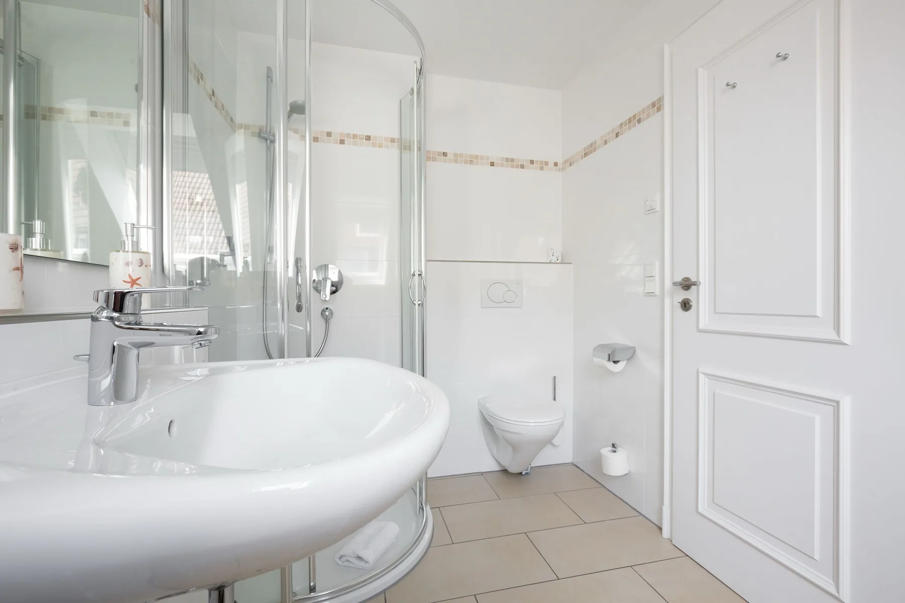 Un baño luminoso con lavabo, ducha e inodoro suspendido.