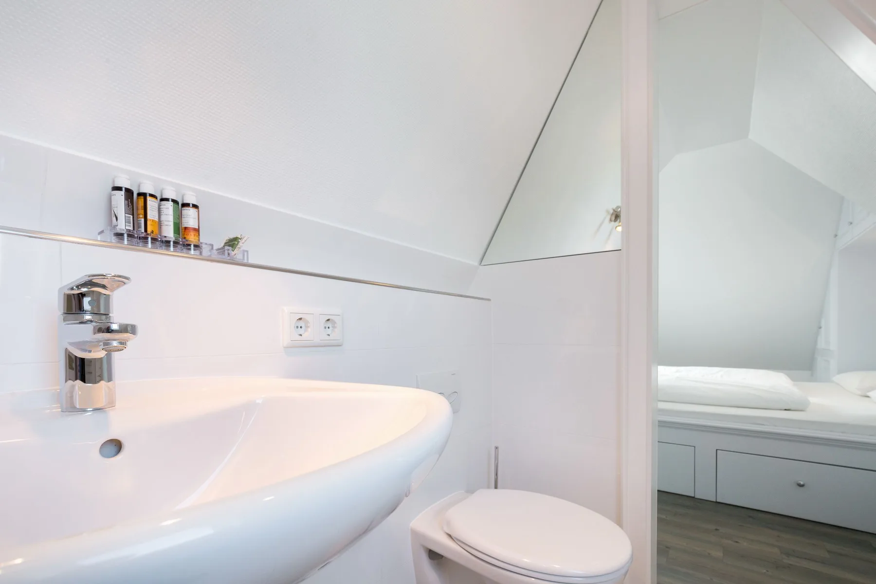 Un baño luminoso con lavabo e inodoro junto a una zona para dormir contigua.