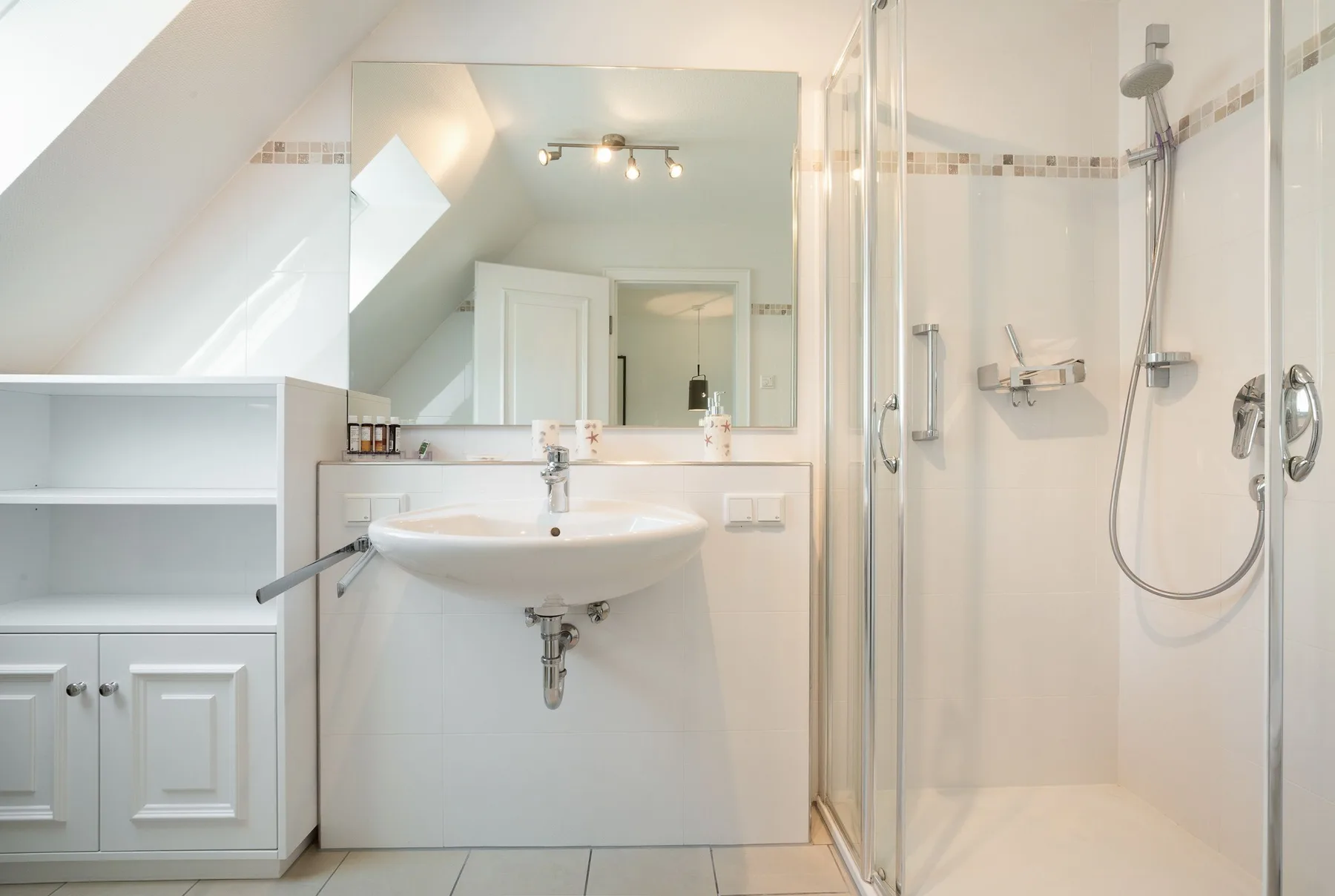 Un baño luminoso con lavabo, espejo y ducha con mampara de vidrio.