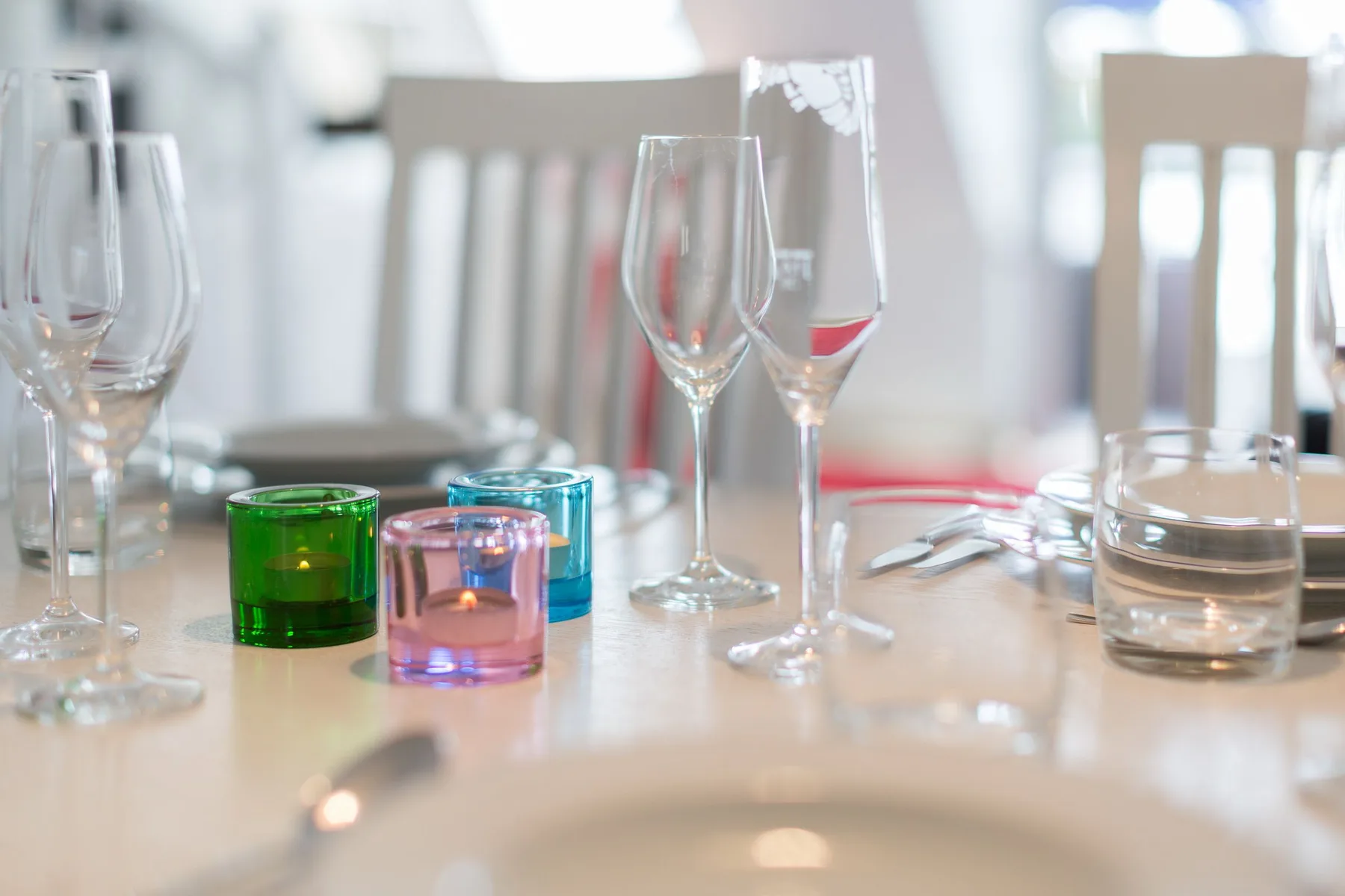 Una mesa de comedor está preparada con copas de vino, portavelas de colores y cubiertos.