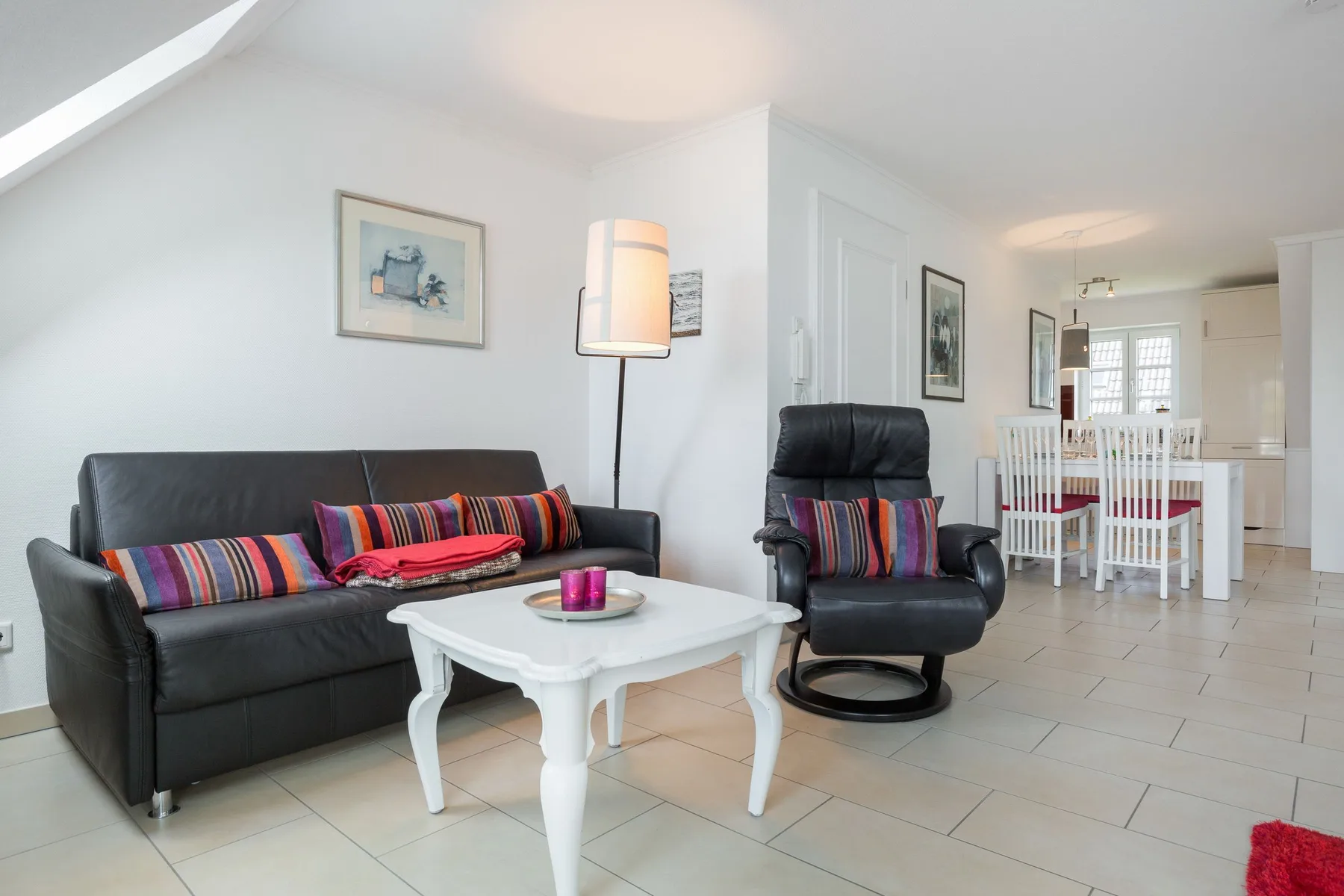 Sala de estar con asientos oscuros y una mesa de centro blanca, con un comedor al fondo.