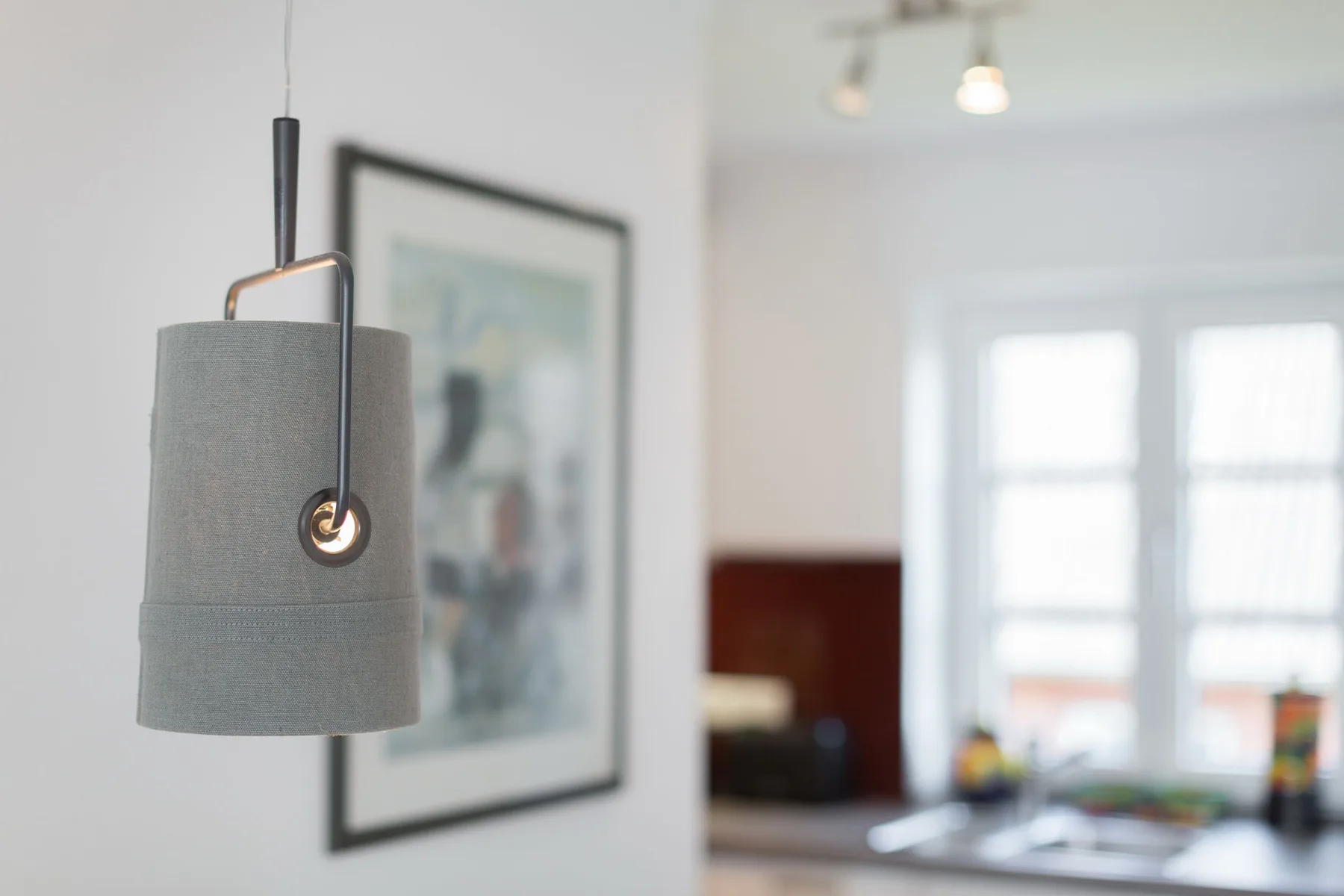 Una lámpara colgante destaca en primer plano en una habitación luminosa con grandes ventanas.