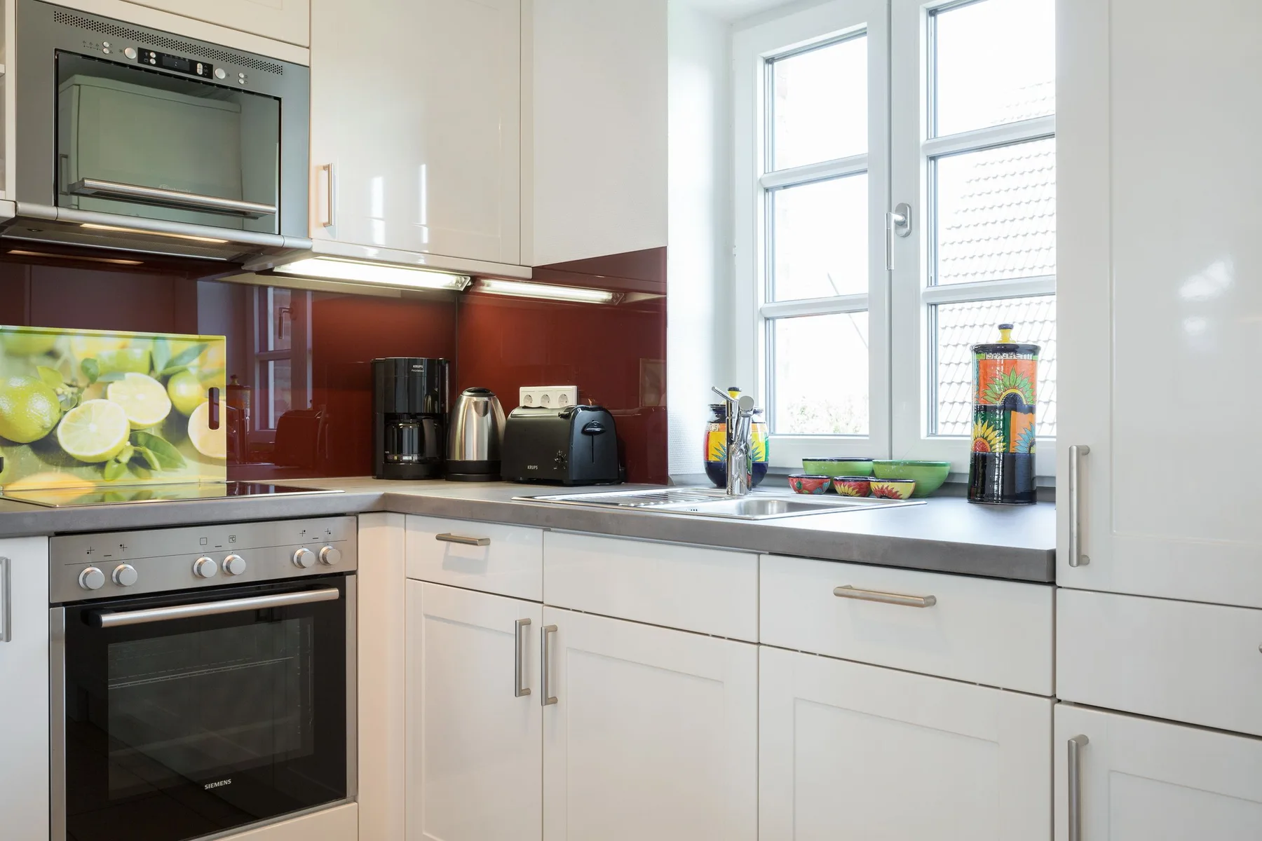 Una cocina moderna y luminosa, con gabinetes blancos y una encimera bajo las ventanas.