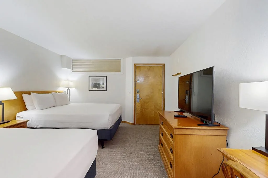 A bedroom with two beds and a television on a wooden dresser.