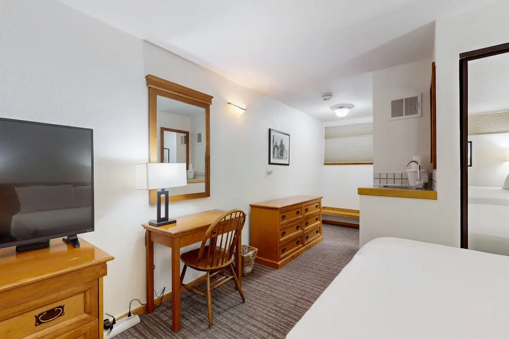A bedroom with a bed, television, and wooden desk.