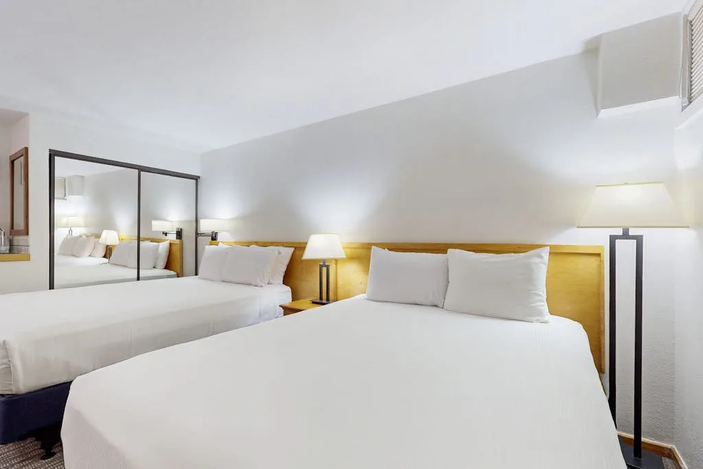 A bedroom with two beds, bedside lamps, and a mirrored wall.