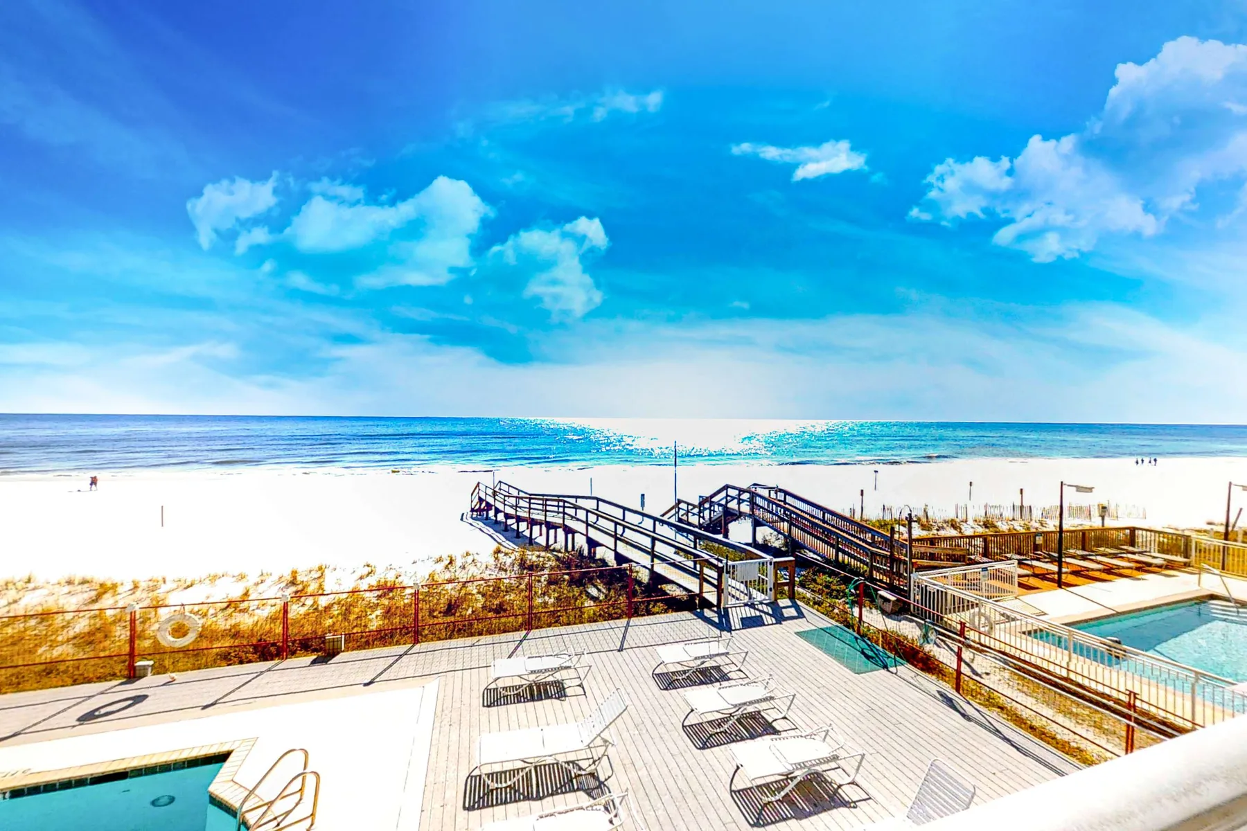 A beachfront pool deck overlooks the ocean, with a wooden boardwalk leading across the sand.