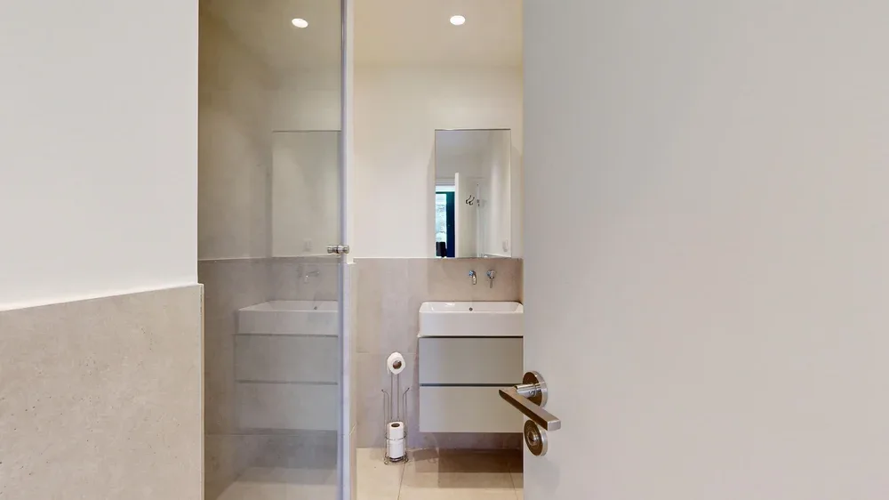 A modern bathroom with a mirrored vanity and pale tiled walls.