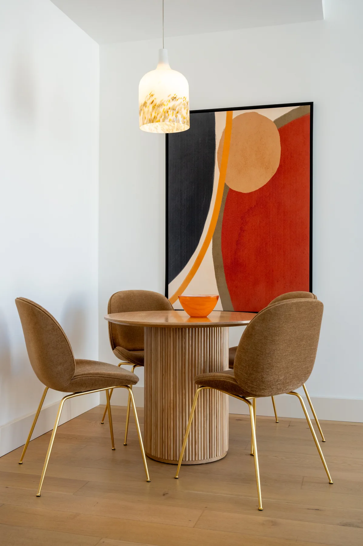 A dining area with a round table, upholstered seating, and a colorful abstract painting.