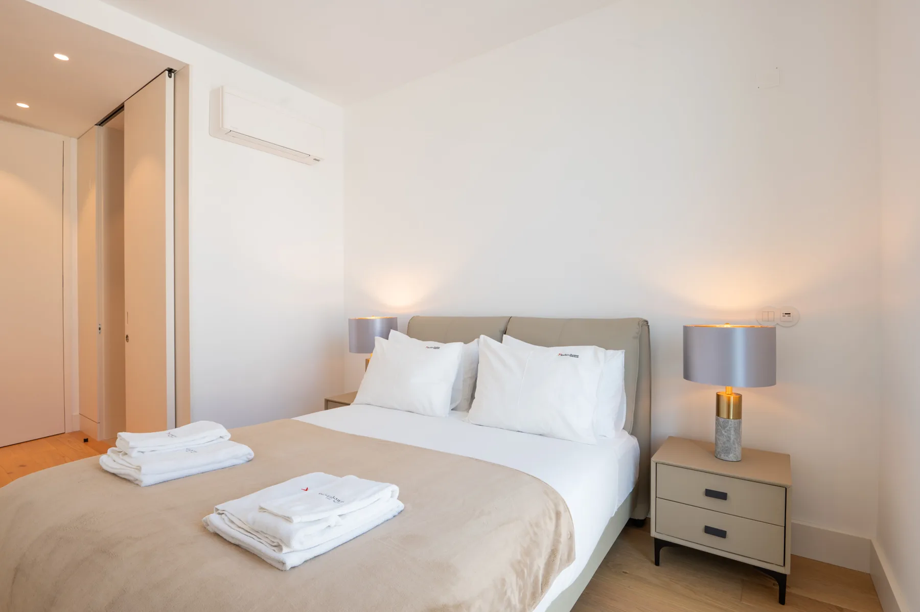 A bright bedroom with a double bed, bedside tables, and folded towels.