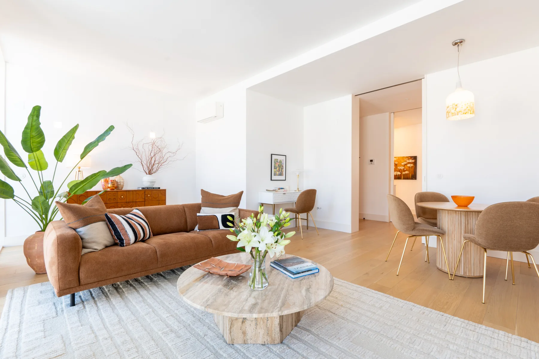 A bright living and dining area with a sofa, table, and indoor plants.