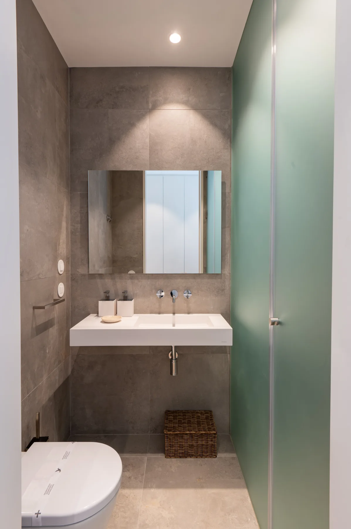 A modern bathroom with a wall-mounted sink, mirror, and glass shower screen.