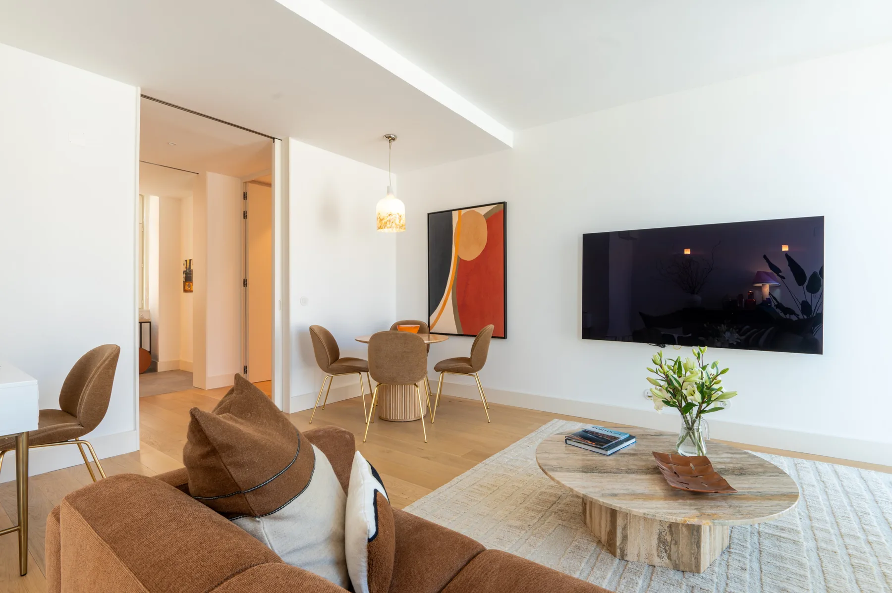 A bright living room with seating, a wall-mounted television, and a coffee table.
