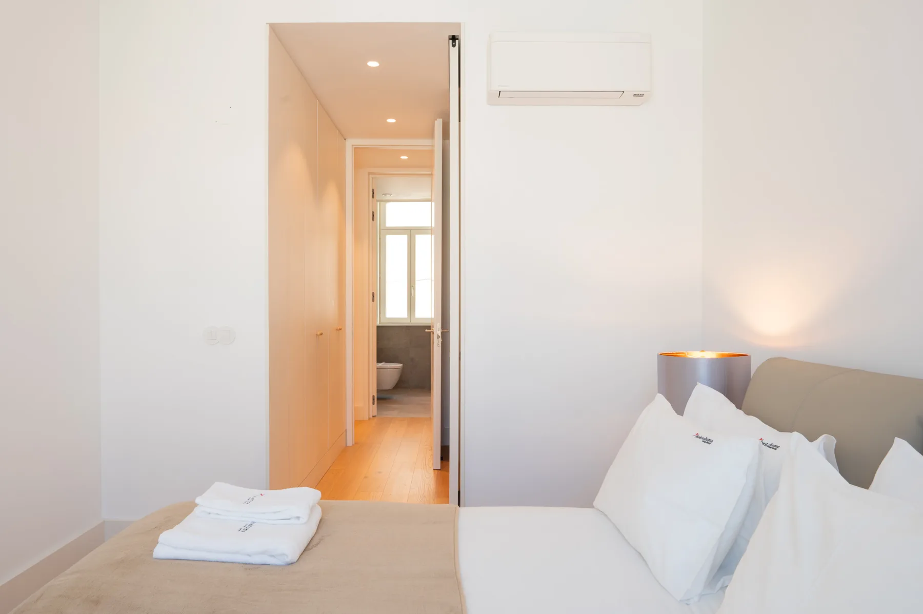 A bright bedroom with a bed, folded towels, and an open doorway to a bathroom.