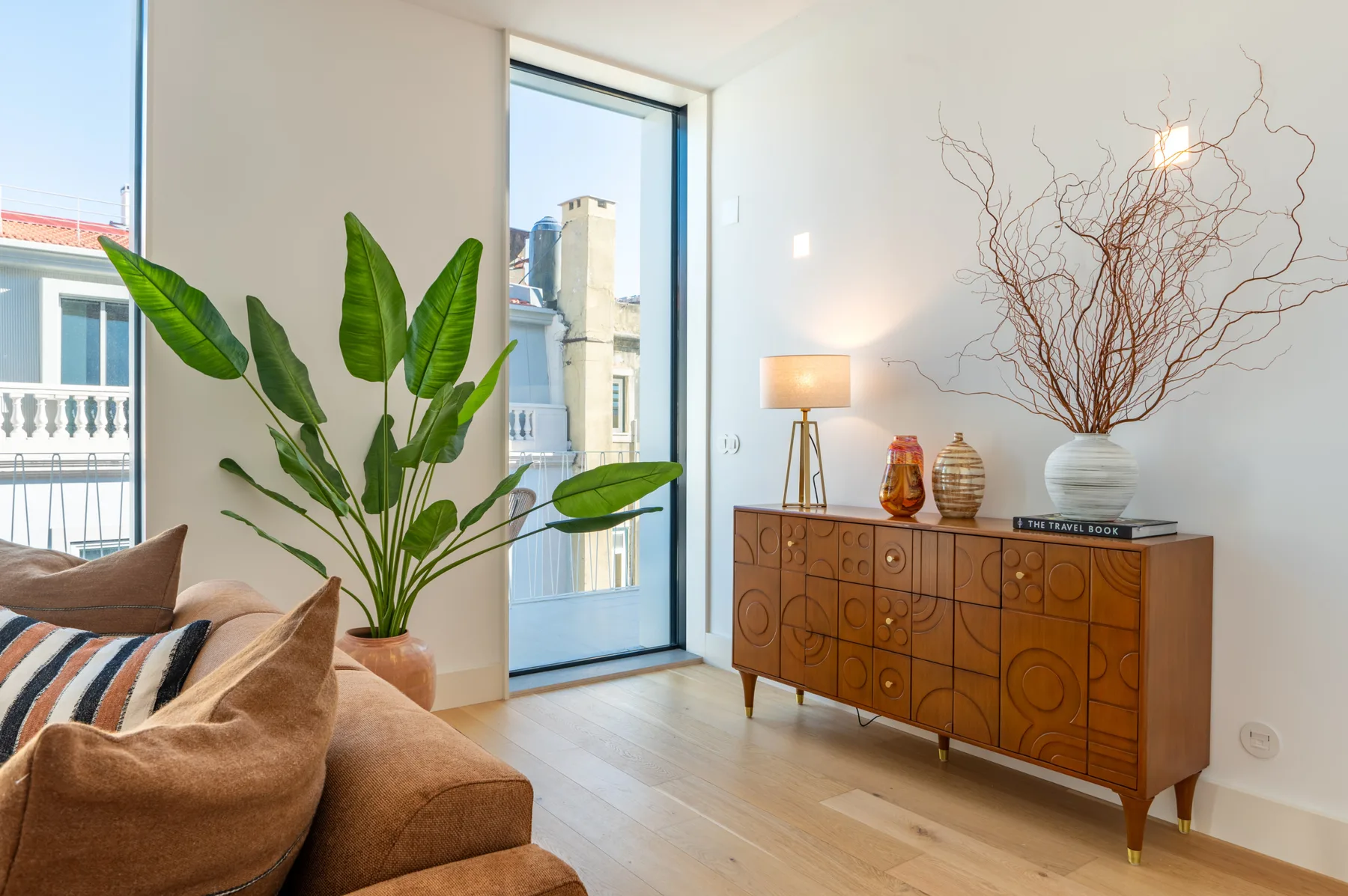 A bright living room with a wooden sideboard, decorative branches, and a potted plant.