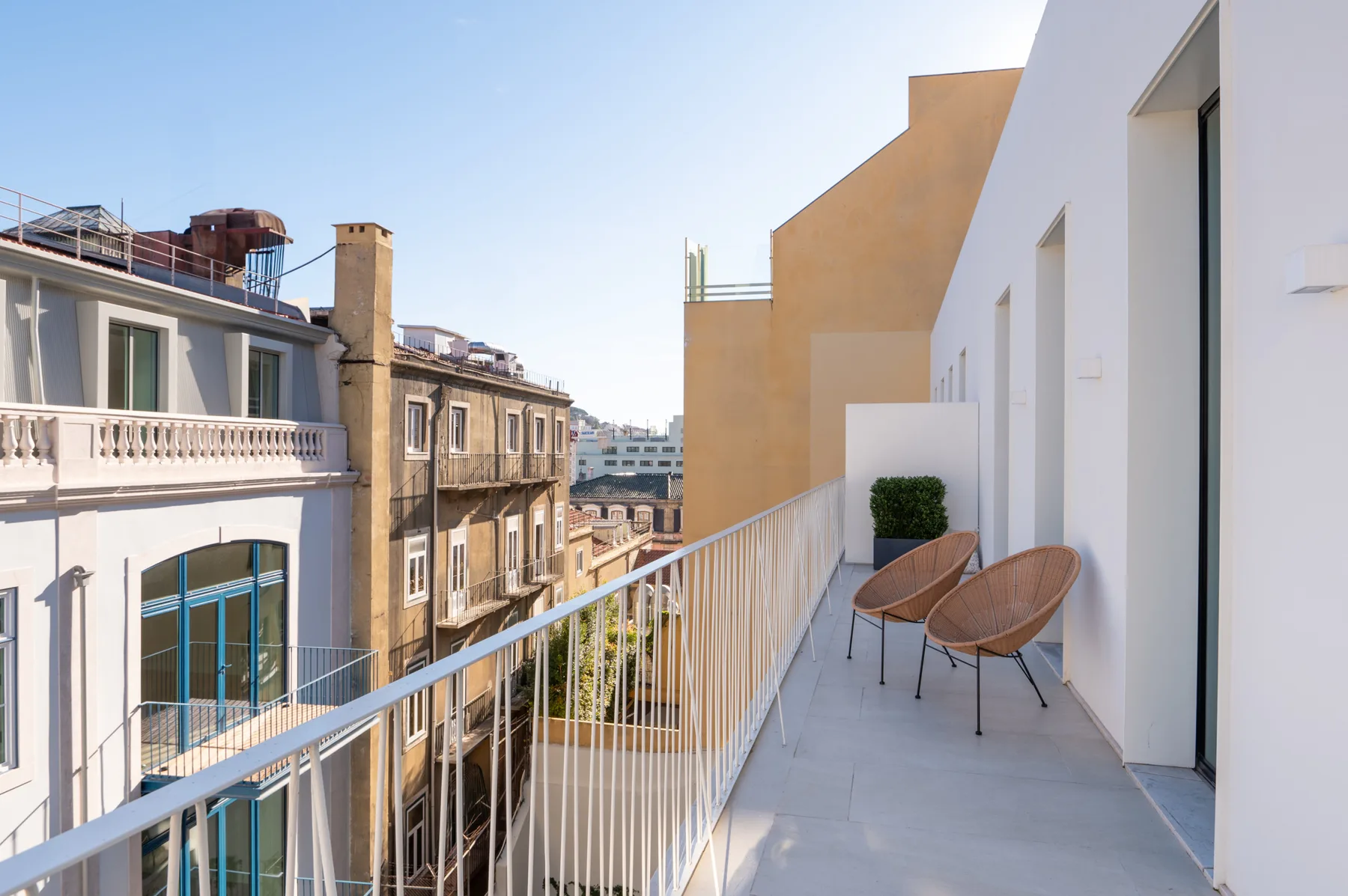 A balcony walkway with two chairs overlooks neighboring city buildings.