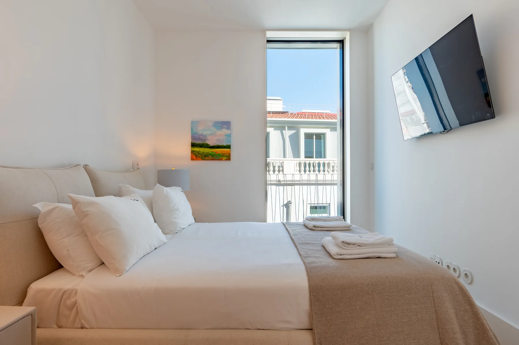 A bedroom with a bed, folded towels, and a wall-mounted television.