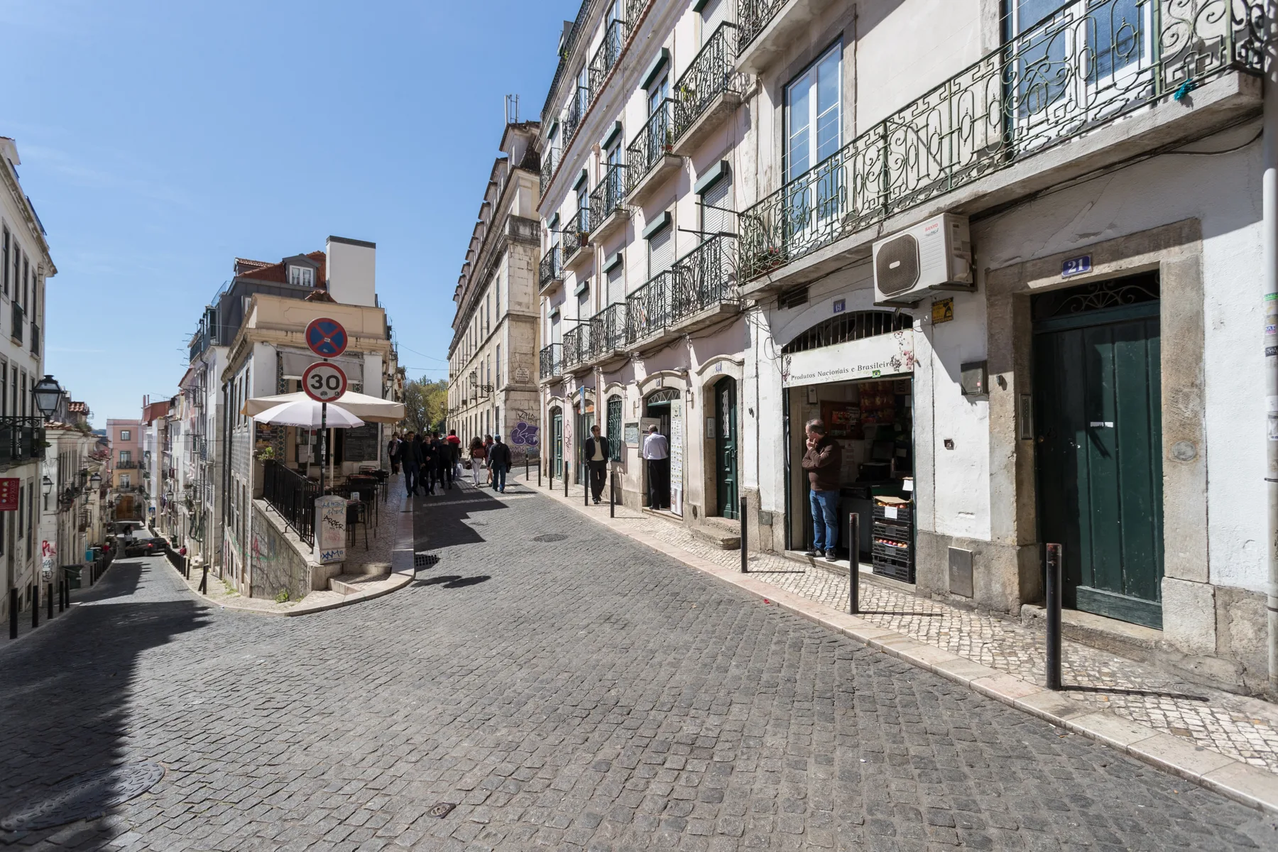Una calle empedrada bordeada de edificios y una pequeña cafetería al aire libre.