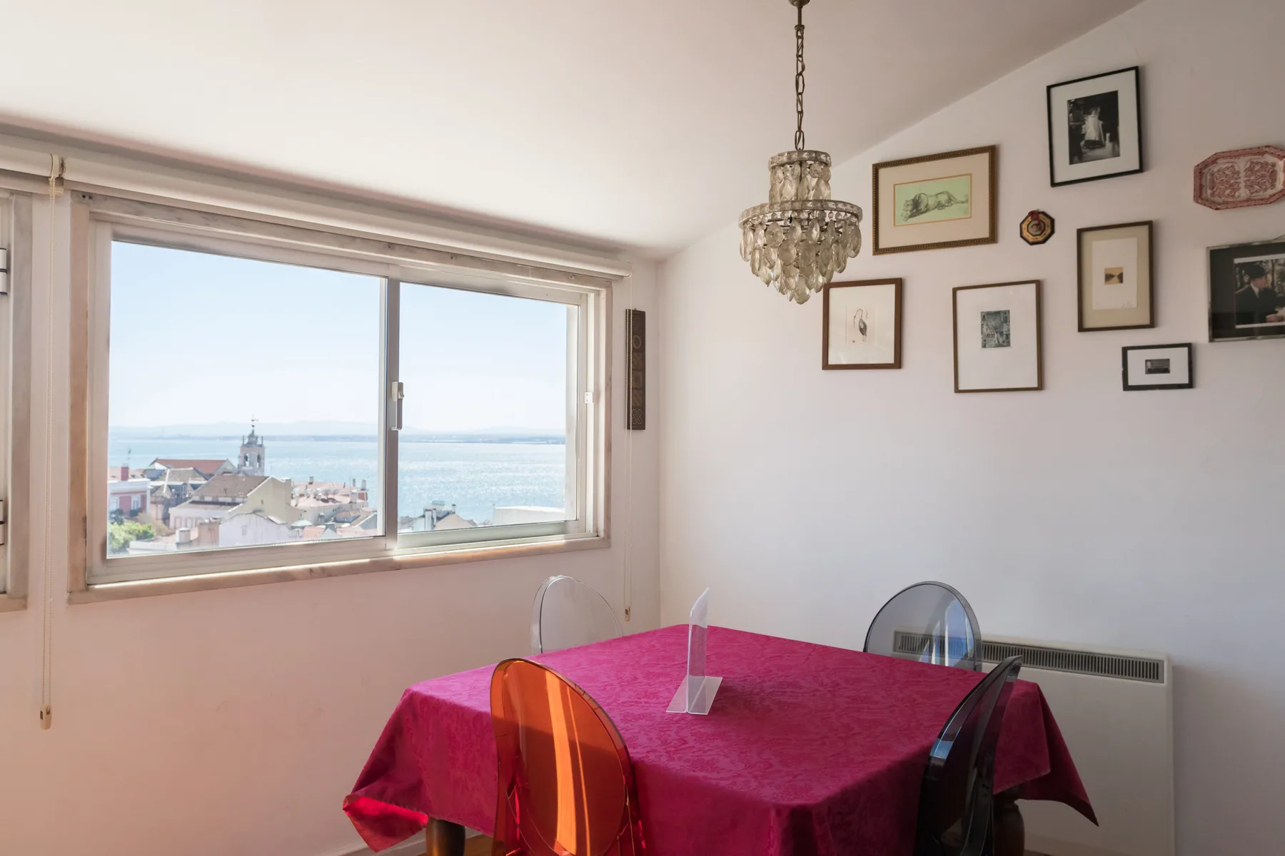 Comedor con una mesa junto a una gran ventana con vistas a tejados y agua.