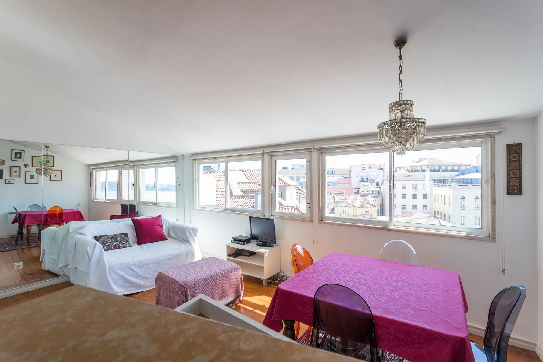 Una luminosa sala de estar y comedor con asientos cubiertos de blanco y una mesa junto a las ventanas.