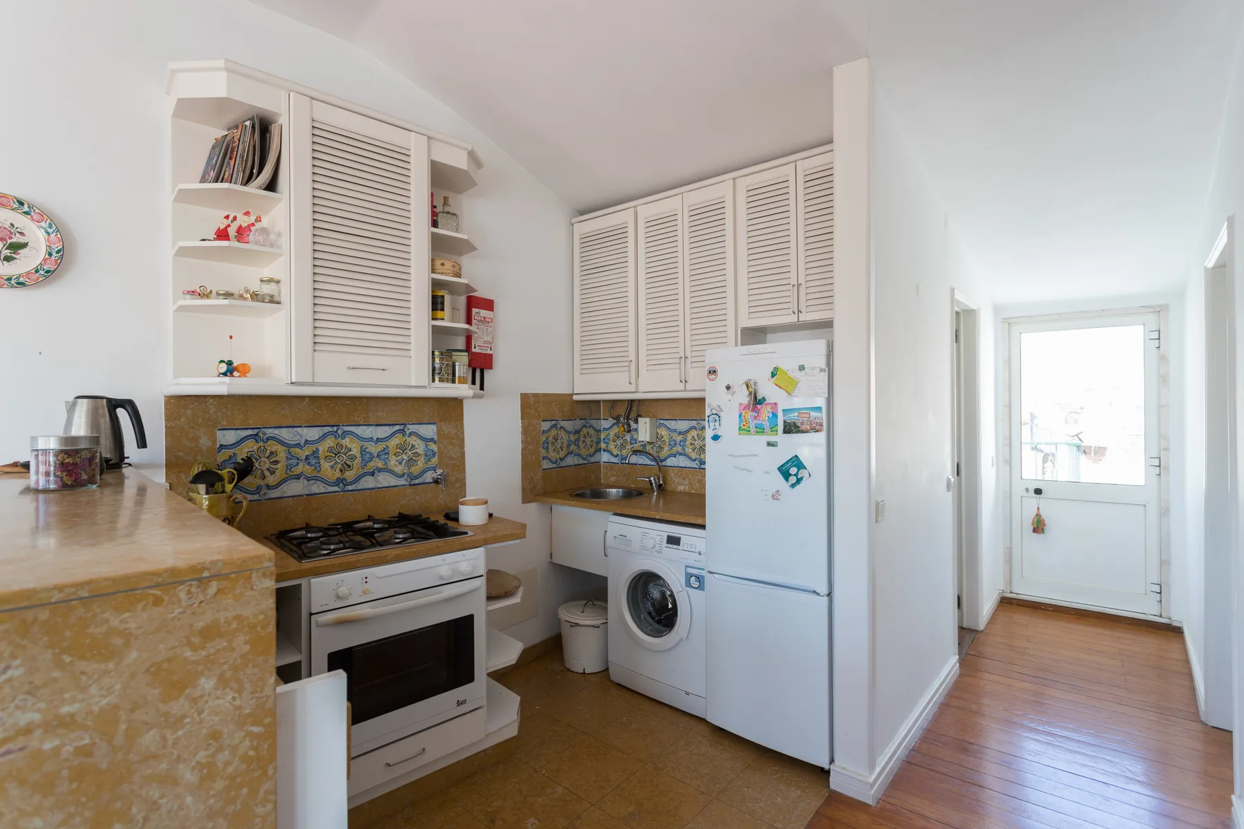 Una cocina compacta con estufa, lavadora y refrigerador junto a un pasillo luminoso.