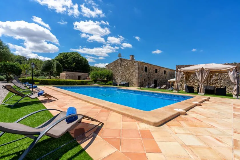 An outdoor swimming pool beside a stone building, with lounge seating on the patio.