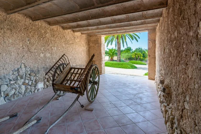 A rustic stone passage opens onto a garden, with a wooden cart inside.