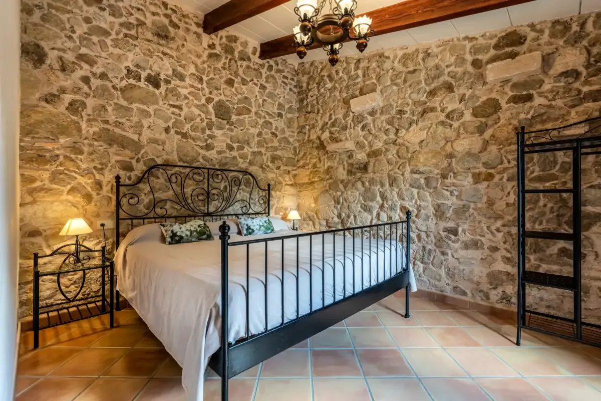 A bedroom with a metal bed, exposed stone walls, and wooden ceiling beams.